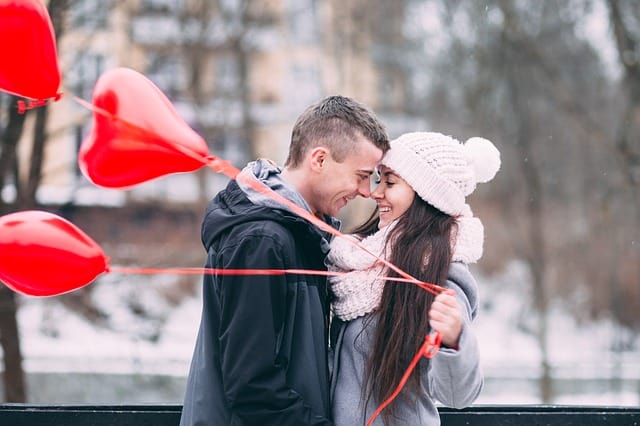 Un couple tenant des ballons rouges dans la neige.